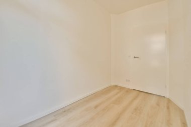 Ahşap zemini ve beyaz duvarları olan boş bir oda. Köşedeki lamba armatürünü ortaya çıkarmak için kapı açık.