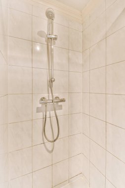 Duş başlıklı beyaz fayanslı bir banyo ve duvardaki parmaklıklar yerdeki seramik fayanslardan yapılmıştır.