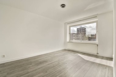 Beyaz duvarları ve ahşap döşemeleri olan boş bir oda. Şehir geneline bakan geniş bir pencere var.