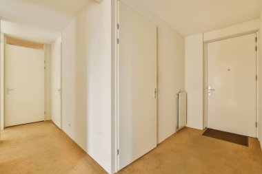 Beyaz duvarları ve ahşap döşemeleri olan boş bir oda. Kapının önü açık. Kapılar kapalı.