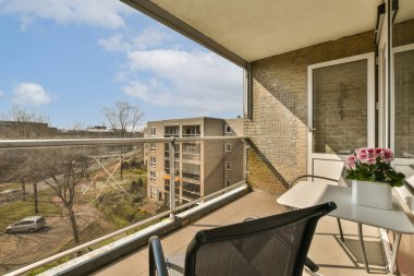 Masasında çiçekler olan bir balkon ve ön verandasından şehre bakan sandalyeler.