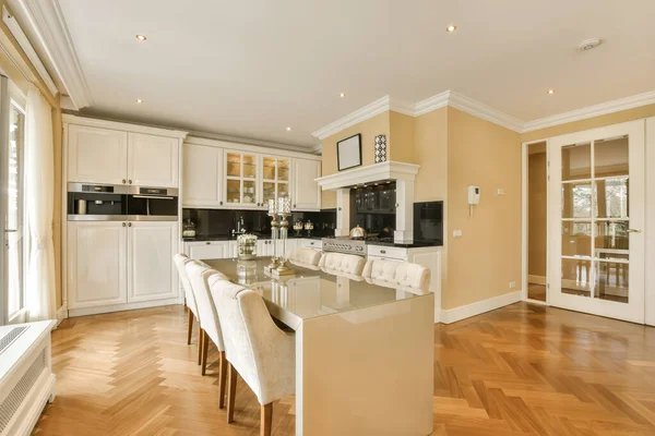 a kitchen and dining area in a home with hardwood flooring, white cabinets and an island bench on the right side