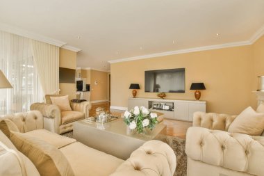 Oturma odası, koltuklar, sandalyeler ve odanın köşesindeki duvarda düz ekran televizyon.