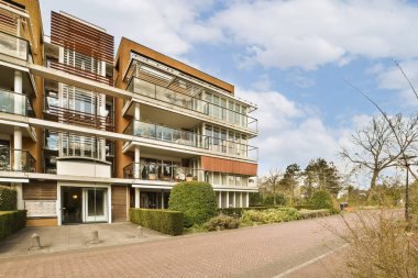 En üst katında bir sürü pencere ve bant olan, ön bahçesinde yeşil çimlerle çevrili bir apartman.