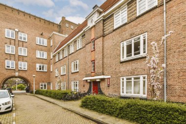 Yolun ortasına park etmiş arabalarla dolu bir tuğla bina ve yol ortasında bir kemer.