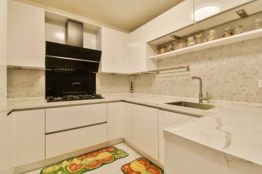 Duvarlarında beyaz dolaplar ve mermer tezgahlar olan bir mutfak alanı ve köşesinde de bir fırın.
