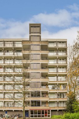 Arabaları caddenin yanına park edilmiş bir apartman dairesi ve park alanında yürüyen insanlar.