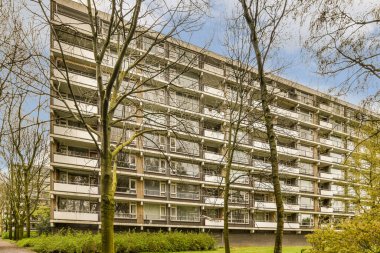 Önünde ağaçlar olan bir apartman dairesi ve park yerinin diğer tarafına park etmiş birkaç araba.