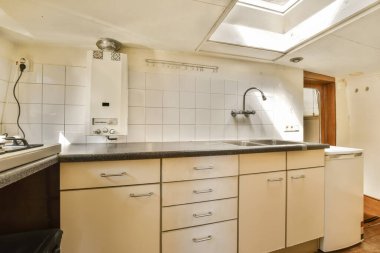 Bu fotoğraftaki tezgahların üzerinde beyaz dolaplar ve siyah tezgahlar olan boş bir mutfak içeriden çekilmiştir.