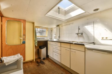 Ahşap döşemeli, beyaz dolaplı, lavabolu ve bulaşık makineli bir evde küçük bir mutfak.