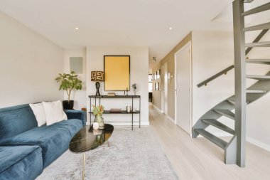 Bu modern tarz apartman dairesinde, ikinci kata çıkan mavi kanepeleri ve merdivenleri olan bir salon.