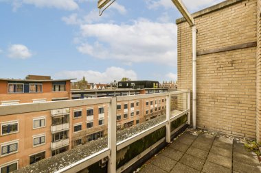 Güneşli bir günde bir balkondan görüldüğü gibi, arka planda bazı binalar ve üzerinde mavi gökyüzü olan bir dış alan.