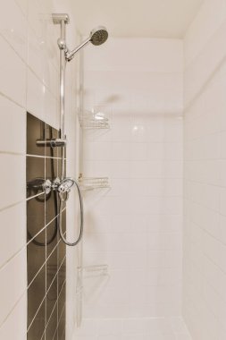 Duvarlarında beyaz fayanslar, küvetin etrafında siyah süslemeler, duş başlığı ve tırabzanlar olan bir banyo.