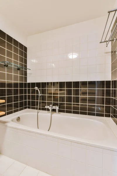 stock image a bathroom with black and white tiles on the walls, tub, sink, and shower head in its corner