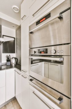 Fotoğrafta beyaz dolapları ve paslanmaz çelikten aletleri olan modern bir mutfak sağda çekiliyor, fakat görünürde yok