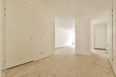 Odanın ortasında beyaz duvarları ve ahşap döşemeleri olan boş bir oda başka bir odaya açılan bir kapı var.