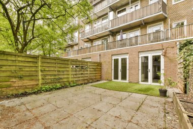 Tuğlalı bir apartmanın önünde, üzerinde ağaçlar ve bitkiler olan bir arka bahçe.