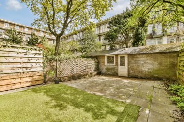 Güneşli bir günde arka bahçesinde çimenler, ağaçlar ve çitler olan bir apartman dairesi.