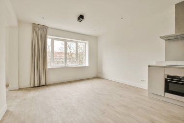Mutfak alanında beyaz duvarları ve ahşap döşemeleri olan boş bir oturma odası sağ tarafta görünüyor.