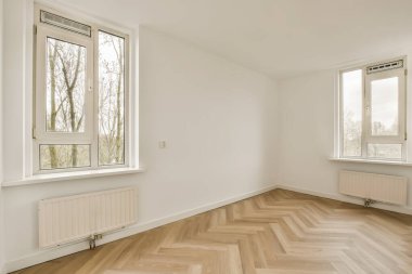 Odanın zemininde boş bir oda ve dışarıdaki ağaçlara bakan iki pencere beyaz.