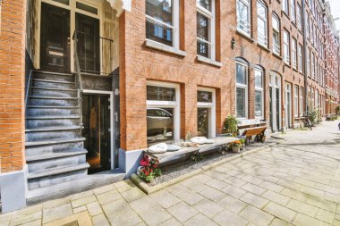 Kaldırımında çiçekler olan tuğla bir bina ve başka bir binaya açılan açık bir kapıya çıkan merdivenler.