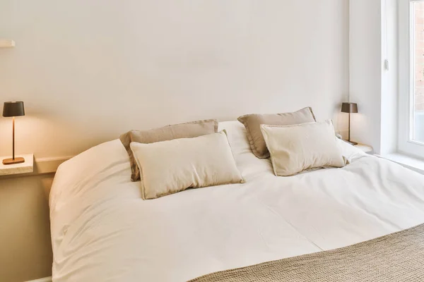 stock image a bed in a bedroom with two pillows on it and a lamp next to the headboard that is lit