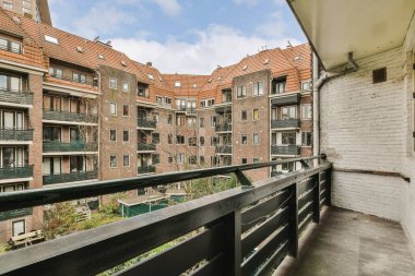 Arka planda binalar ve üzerinde mavi bir gökyüzü olan bir balkon, bir apartmanın balkonundan alındı.