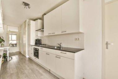 Lavabonun önündeki adada beyaz dolapları ve siyah tezgahları olan bir mutfak ocağın yanındadır.