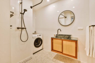 Modern bir banyo mermer döşemeli ve lavabonun yanındaki duvara siyah banyolu duş başlığı monte edilmiş.