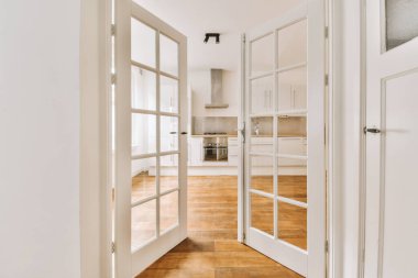 Beyaz duvarları ve ahşap döşemeleri olan boş bir oda, kapıdan mutfak alanına kadar açık.