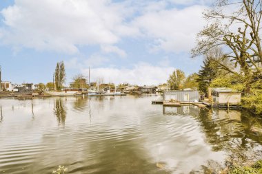 Arka planda evleri olan bir göl ve suya yansıyan ağaçlar, güneşli bir günde sadece bulutlu.