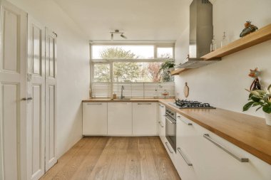 Lavabonun önündeki tezgahlarda beyaz dolaplar ve ahşap tezgahlar olan bir mutfak dışarıya açıktır.