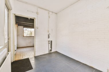 Duvarında beyaz tuğlalar ve açık kapının önünde yerde siyah fayanslar olan boş bir oda.