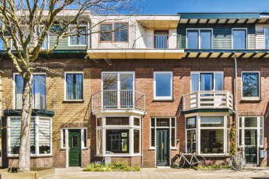 Önünde bir sürü pencere ve balya bulunan tuğla bir bina büyük bir ağaçtır.