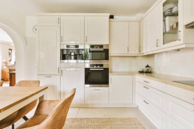 Tezgahında beyaz dolaplar ve aletler olan açık bir alanda yemek alanı olarak kullanılan bir mutfak.