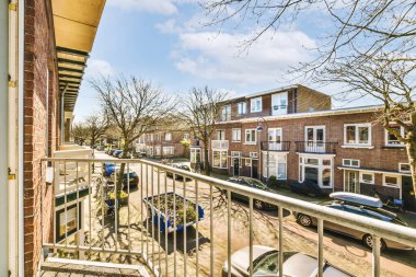 Dışarıda park halindeki arabaların olduğu sokağa bakan sandalyeler, masalar ve şemsiyelerle dolu bir balkon.