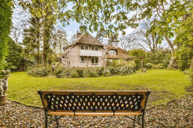 Bahçenin ortasında bir bank. Arka planda bir ev var. Etrafında da terk ediyor.