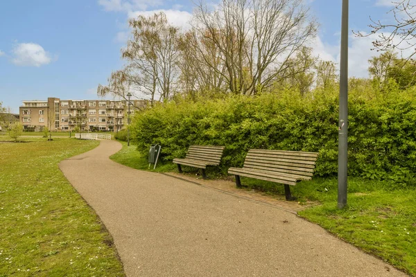 stock image a park bench in the middle of an urban area with trees and bushes on either side of the path that leads to apartment buildings