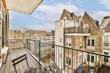 Dışında sandalyeler ve şemsiyeler olan bir balkon, binaların birinden sokağa bakıyor.