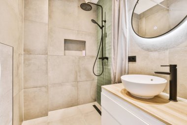 Lavabosu, aynası ve duş başlığı olan bir banyo. Duvara monte edilmiş küvetin yanında.