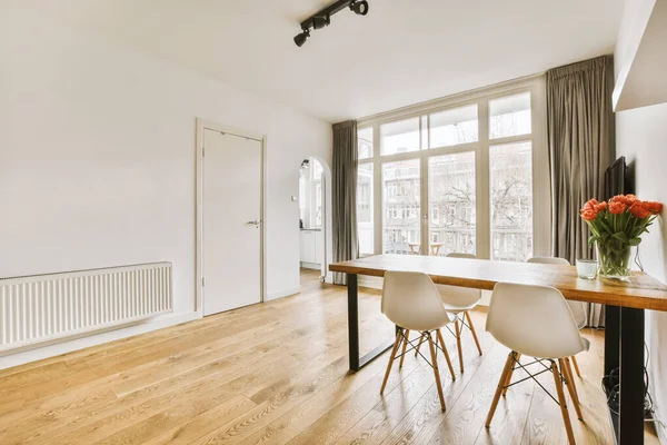 木製の床と白い壁と大きな窓のあるリビングルームのダイニングテーブルと椅子が通りを眺めながら — ストック写真