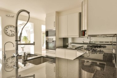 Tezgahta saati olan bir mutfak ve arkada lavabonun yanındaki fırın beyazdır.