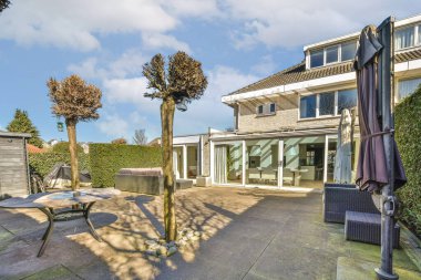 Güneşli bir günde evin önünde sandalyeler, masalar ve şemsiyelerle dolu bir teras.