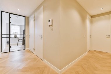 Her iki tarafında tahta döşemeleri ve beyaz duvarları olan boş bir oda. Köşesinde bir kapı var.