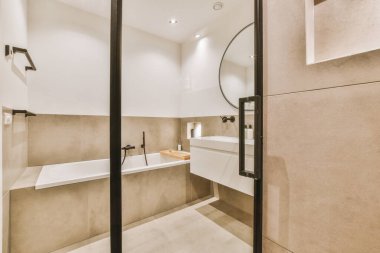 Bej duvarları ve yerde beyaz fayansları olan modern bir banyo. Duvarda büyük bir ayna var.