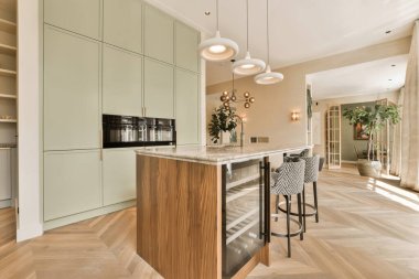 Odanın ortasında ahşap döşemeli ve açık yeşil dolaplı modern bir mutfak bir adadır.