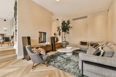 Ahşap döşeme ve duvarlarında bej duvar kağıtları olan bir oturma odası. Bir kanepe, sehpa ve iki sandalye var.