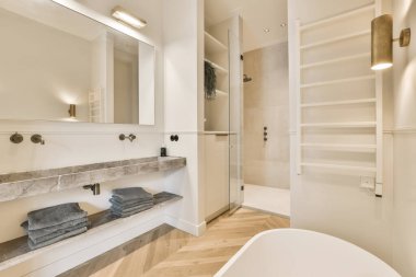 Ahşap döşemeli, beyaz duvarlı, mermer tezgahlı ve aynalı modern bir banyo.