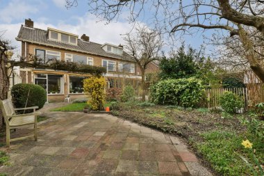 Ön bahçesinde ağaçlar ve her iki tarafında çalılar olan bir ev, boş bir bahçe alanı var.