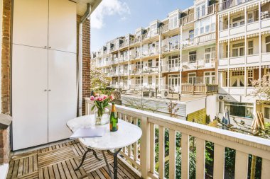 Bir apartmanın önündeki masanın üzerinde sandalyeler, masalar ve çiçekler olan bir balkon.